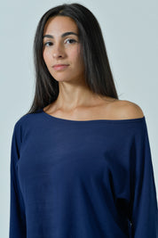 Modella di tre quarti con la maglia blu navy, scollo a barchetta scivolato sulla spalla